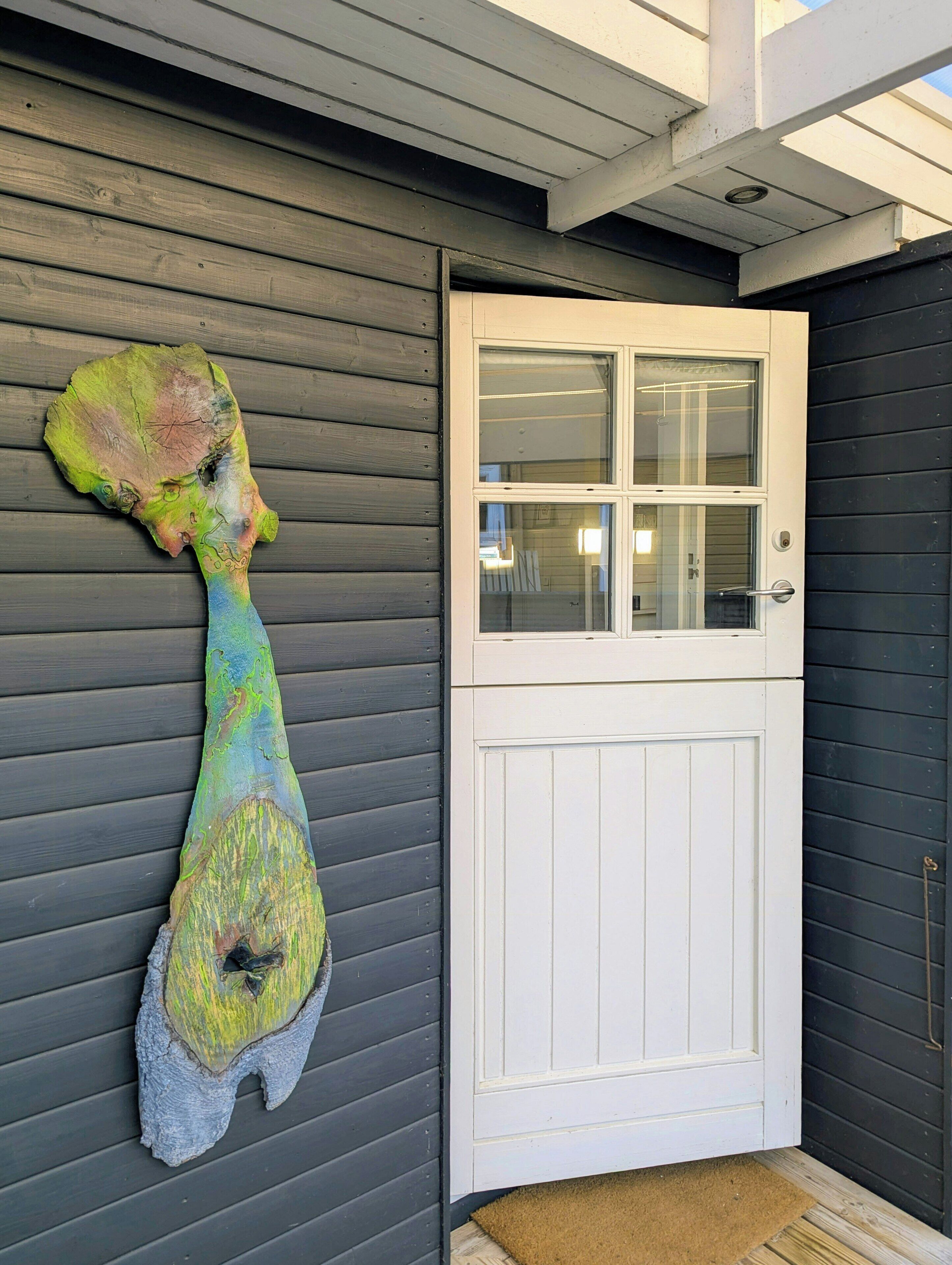 Et hus med hvid dør, stort vindue og en unik skulptur på væggen.