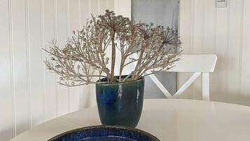 A white table with a blue vase containing dried branches and a bowl of pebbles.