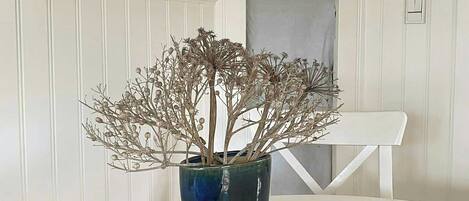 A white table with a blue vase containing dried branches and a bowl of pebbles.