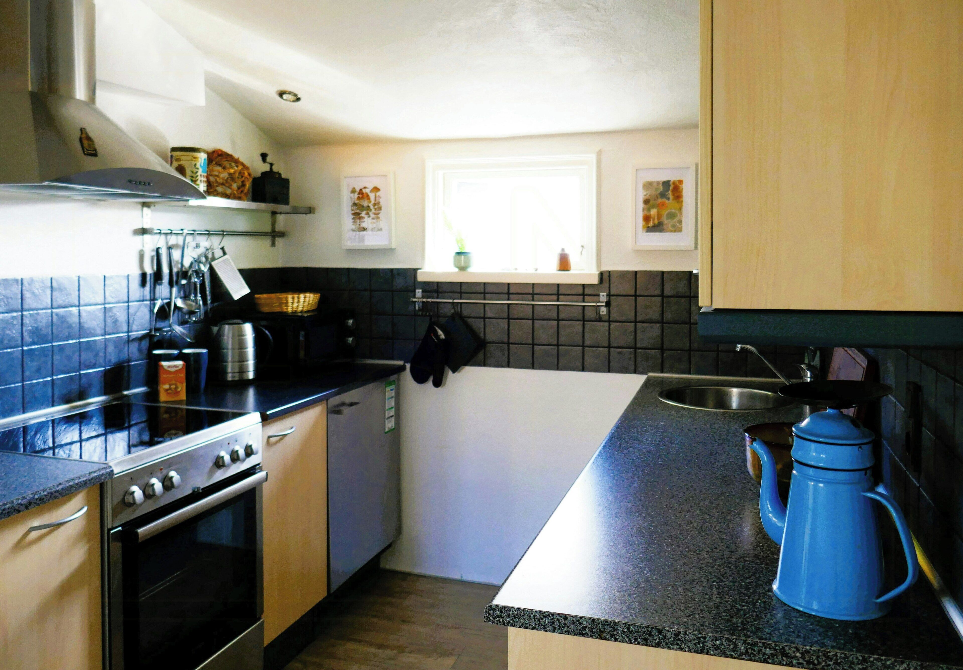 A compact kitchen with a stove, oven, sink, and a blue kettle.