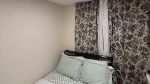 Een slaapkamer met een bed, bloemen gordijnen, een geruit sprei en een plafondlamp.