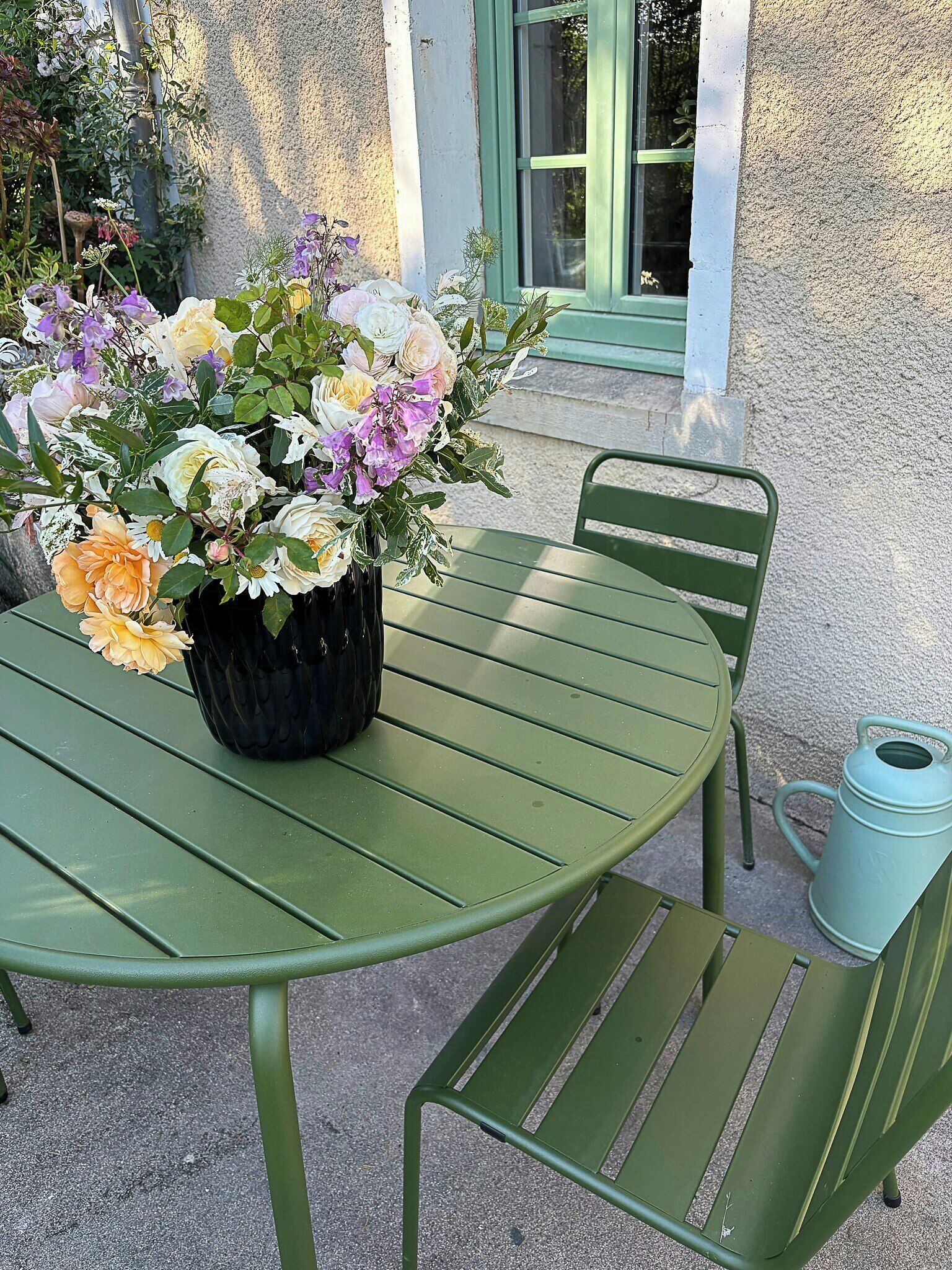 Una mesa metálica verde con un jarrón negro de flores.