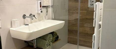 Un baño moderno con cabina de ducha de vidrio, un lavabo blanco y un estante de madera.
