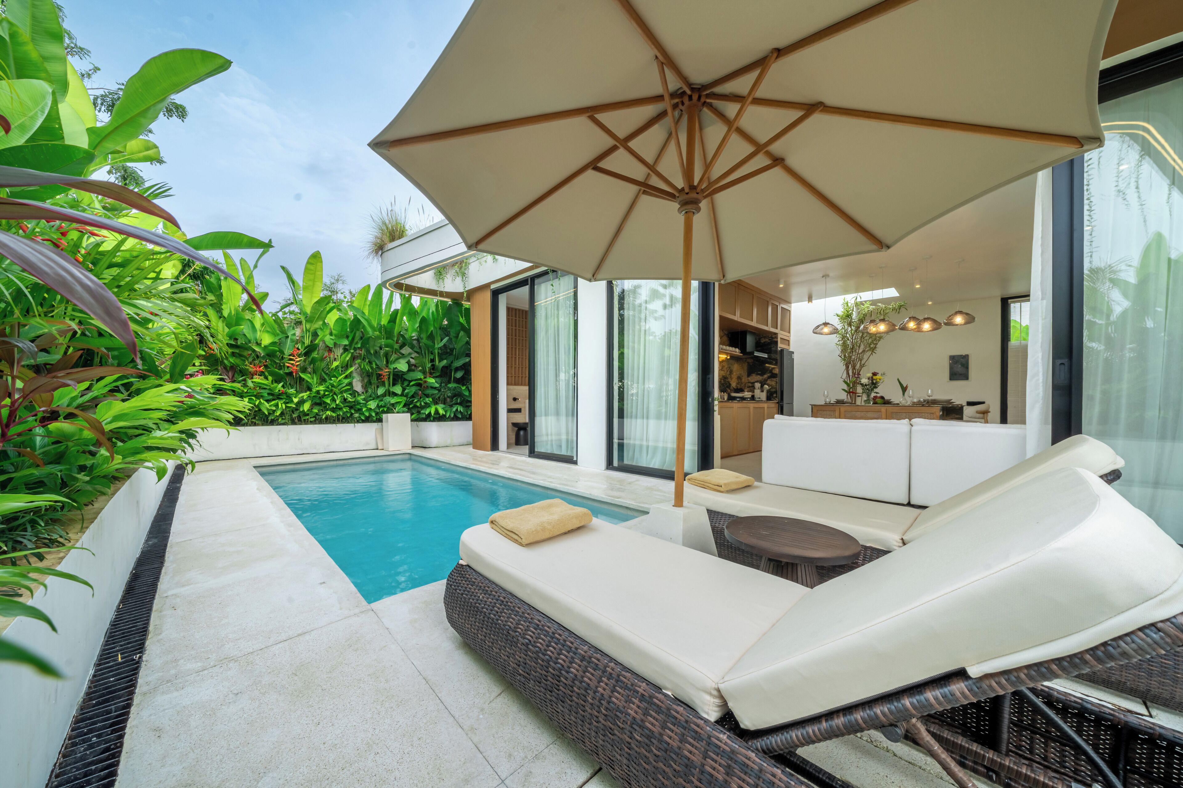 A poolside area with lounge chairs, a large umbrella, and lush greenery.