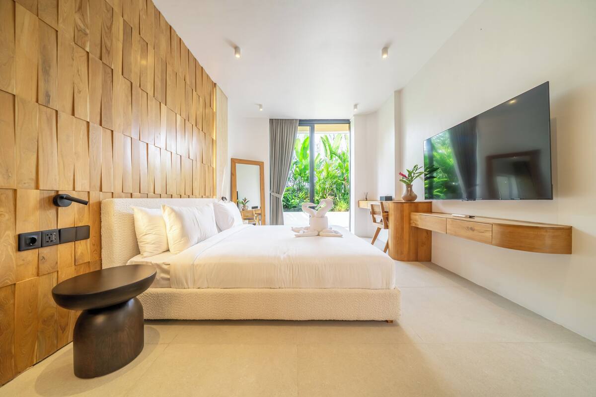 Un dormitorio moderno con una cama grande, panel de madera en la pared, televisión y vistas a zonas verdes.