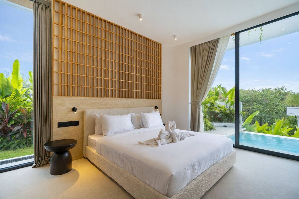 Habitación de hotel moderna con una cama grande, vista a una piscina y un separador de pared de madera.