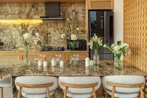 Una cocina con encimera de mármol, sillas blancas y un mueble de madera.