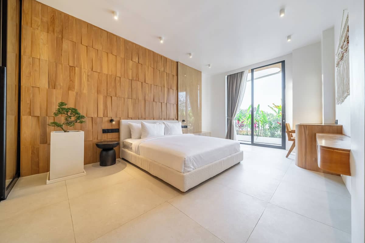 Un dormitorio moderno con panel de madera, cama, mesita de noche, planta en maceta y vistas a zonas verdes.