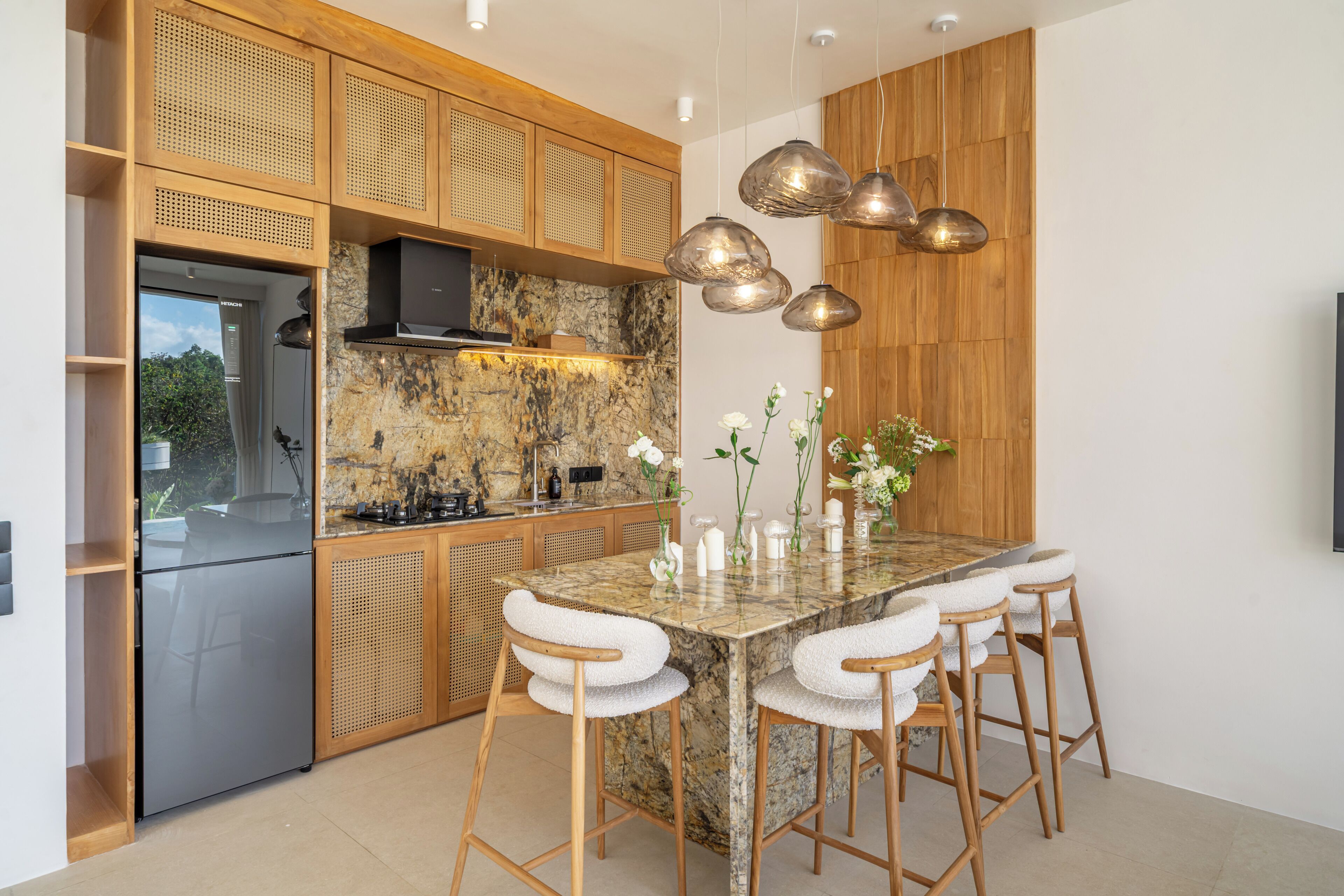 A modern kitchen with a marble island, wooden cabinetry, and pendant lighting.