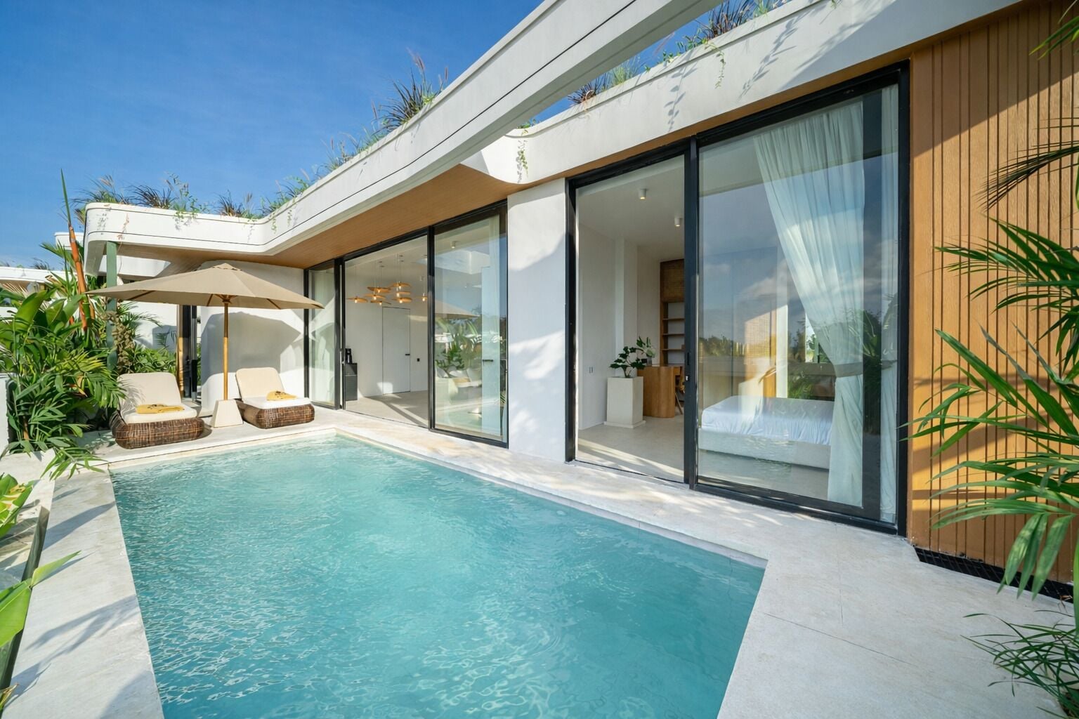 Ein modernes Haus mit Schwimmbad, Schiebetüren und einer Terrasse mit Liegestühlen.