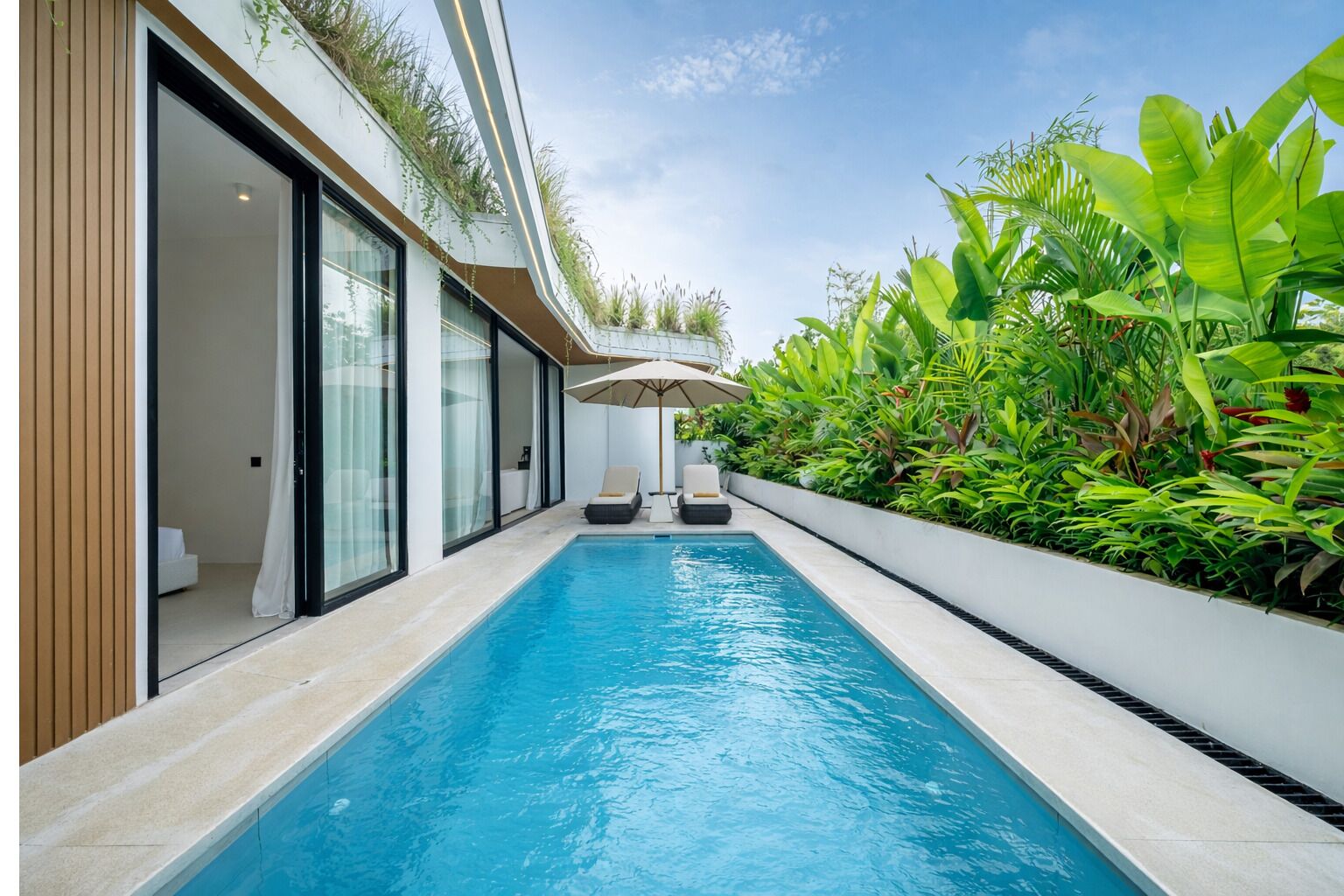 A modern pool area with a clear blue pool, a lounge chair, and a large umbrella.