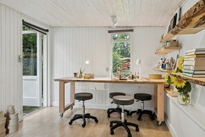 Una habitación con un escritorio de madera, tres sillas de oficina, una ventana y estanterías con libros y un jarrón de flores.