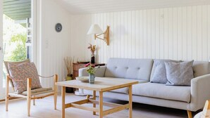 Ein Zimmer mit einer Couch, einem Holztisch, einem Korbsessel und einer Lampe.