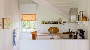 Eine Küche mit weißen Wänden, einem Fenster mit Jalousien, einem Holzregal mit Küchenutensilien und einem Waschbecken mit Armatur.