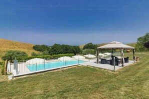 A swimming pool with a covered seating area, surrounded by a fence and a grassy landscape. - Lovely apartment with pool in Chianti (Montaione)