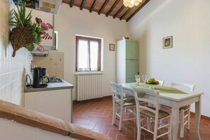 A dining area with a white table, chairs, a green cabinet, and a window with curtains. - Lovely apartment with pool in Chianti (Montaione)