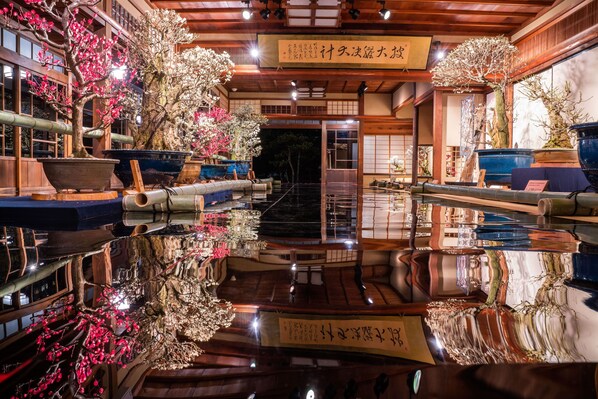 Un interior japonés tradicional con un suelo pulido que refleja la decoración de la habitación, incluyendo bonsáis y elementos de madera.