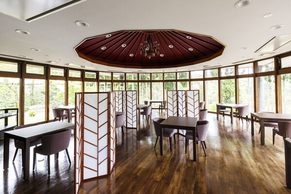 A spacious dining area with wooden flooring, multiple tables and chairs, and large windows offering a view of greenery. - sankennoyado kinomoto (Nagahama)