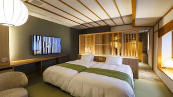 A hotel room with a large bed, a flat-screen TV mounted on the wall, a wooden headboard, and a traditional Japanese-style partition.
