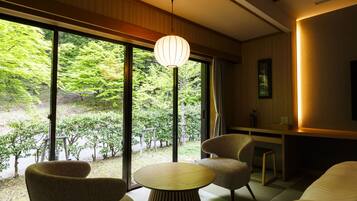 A modern room with large windows, a round table, two chairs, a hanging light fixture, and a small bedside table.