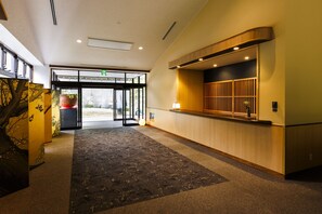 A hotel lobby with a reception desk, a carpeted floor, and a glass door entrance.