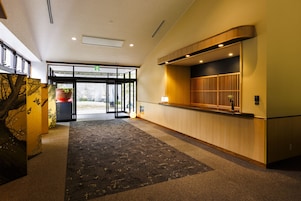 Un vestíbulo de hotel con mostrador de recepción, piso alfombrado y puerta de cristal de entrada.