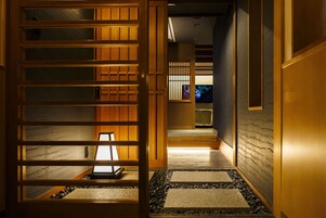 Un pasillo con puertas correderas de madera, un sendero de piedra y una lámpara encendida.