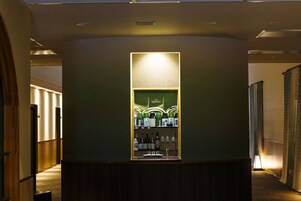 Zona de bar con barra y estanterías llenas de botellas, ubicada en un pasillo con paneles de madera y suelo alfombrado.