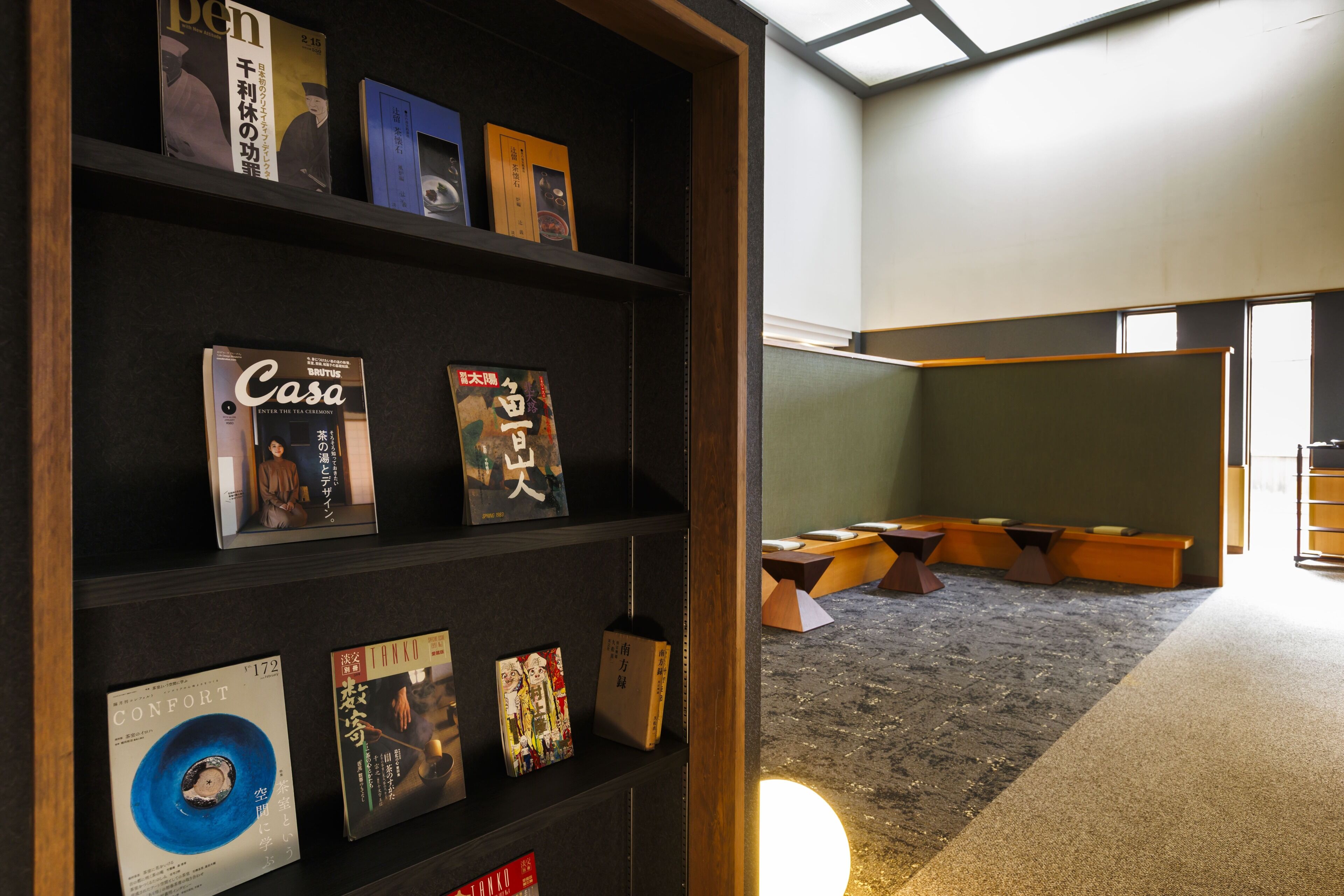 A room with a bookshelf containing various books and a seating area with tables and chairs.