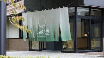 A building entrance with a green banner hanging over the door, a tiled ground, and a glass facade.