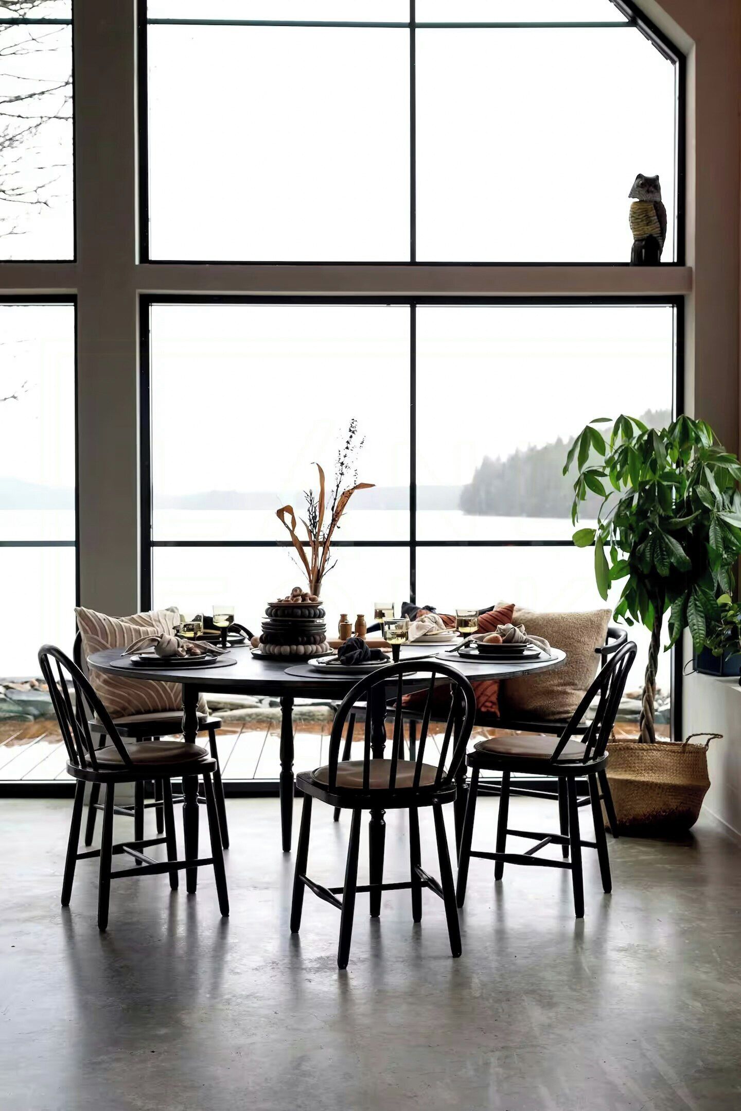A dining area with a large window, a round table, four chairs, and a potted plant.