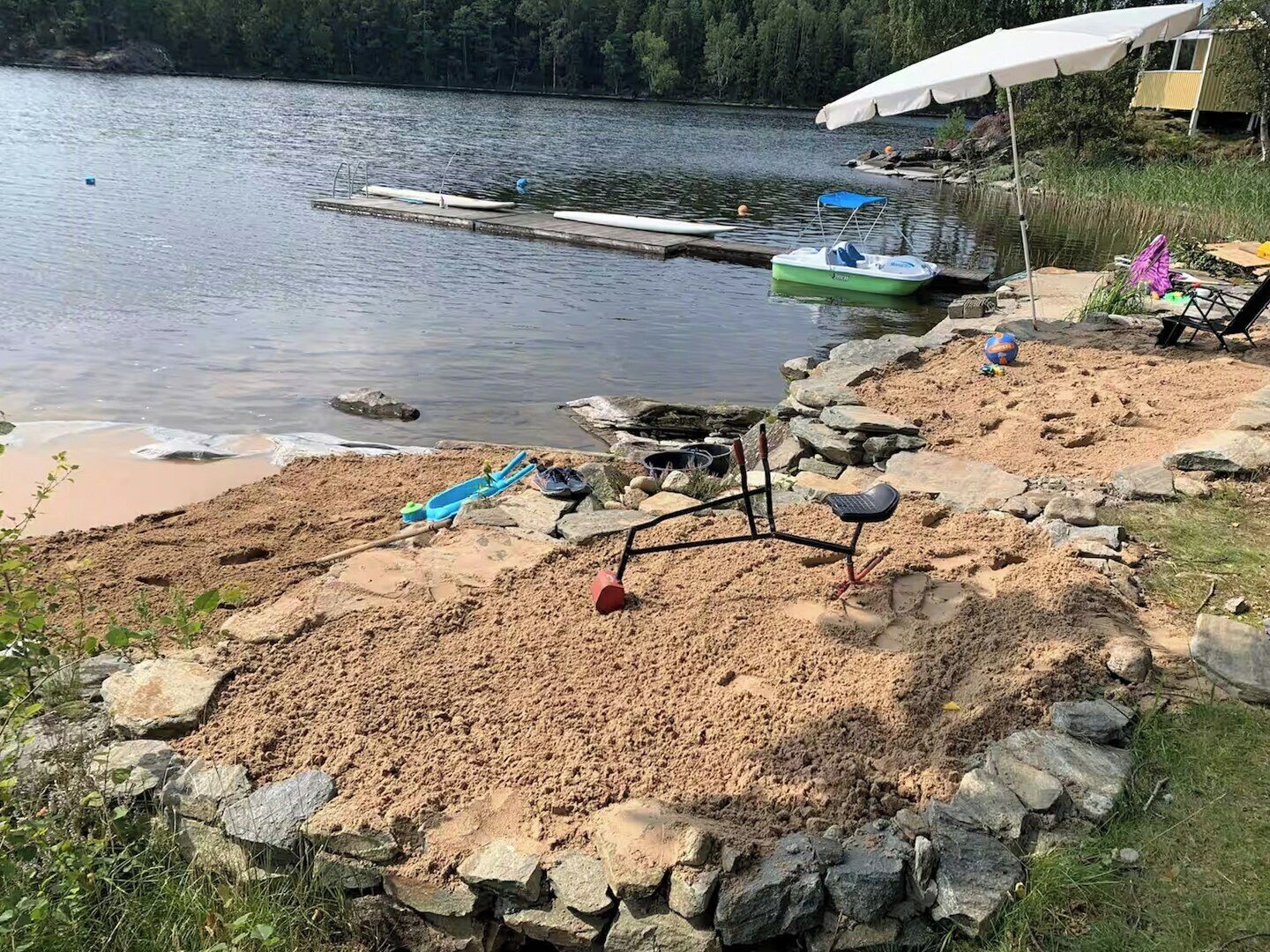 Un cadre idyllique au bord du lac, avec une plage de sable, un quai où sont amarrés des bateaux et une tente.