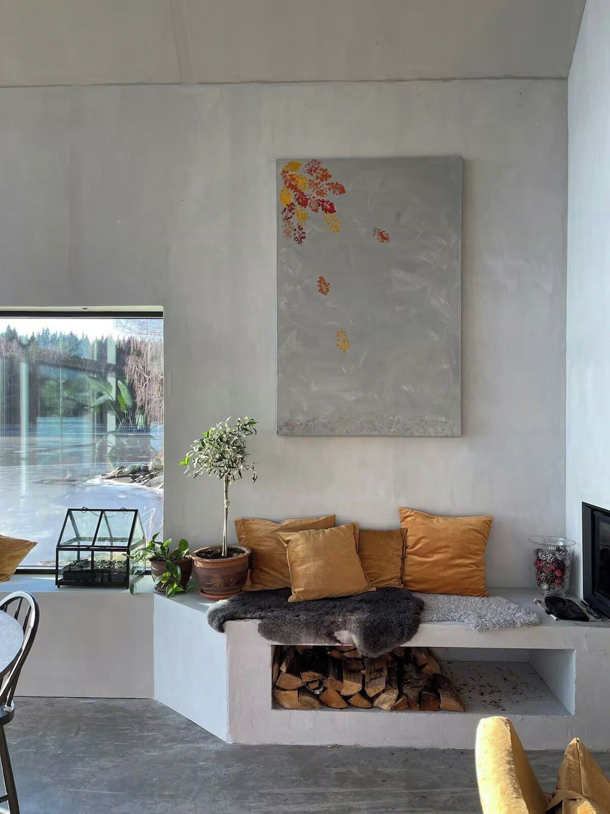 A modern living room with a sofa, cushions, a potted plant, a fireplace, and a large abstract painting on the wall.