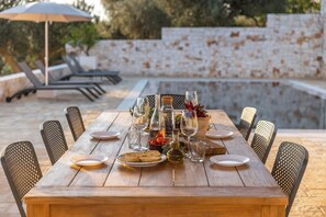 A wooden dining table set outdoors with chairs, glasses, plates, and a bowl of fruit. - Historic trullo in Puglia (Ostuni)