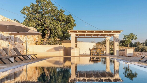 Een zwembad met een pergola, ligstoelen en een stenen muur.