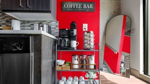 Una cuina amb barra de cafè, rentaplats, cafetera i estanteria amb pots i tasses.