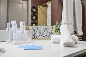 Ein Badezimmer mit Handtuchhalter, einem gerahmten Schild mit der Aufschrift 'hello sunshine' und Pflegeprodukten auf der Ablagefläche.