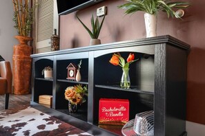 Une console noire avec des étagères, une boîte rouge de la collection « Bachelorette Bundle », et un vase contenant des tulipes orange.