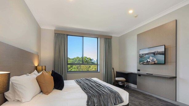 Quarto de hotel moderno com uma cama grande, televisão na parede e janela com vista para a cidade.