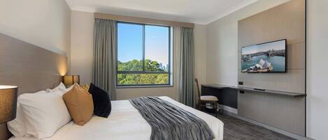 Une chambre d’hôtel moderne, dotée d’un grand lit, d’un téléviseur fixé au mur et d’une fenêtre offrant une vue sur le paysage urbain.