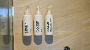 Três frascos brancos de produtos de banho do hotel sobre uma prateleira de vidro.
