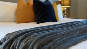 Cama bem arrumada com um cobertor cinza, um travesseiro amarelo e um travesseiro azul escuro.