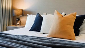 Ein ordentlich bezogenes Bett mit grauer Decke, einer Nachttischlampe und einem Nachttisch.