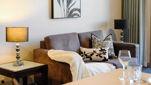Ein Wohnzimmer mit einer Couch, einem Beistelltisch mit Lampe, einem Weinglas und einem gerahmten abstrakten Kunstwerk an der Wand.