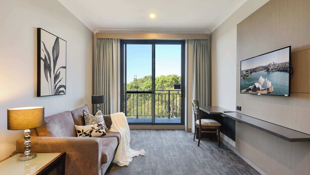 Ein Hotelzimmer mit Balkon, einer Couch, einem Schreibtisch und einem Fernseher.