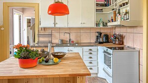 Een keuken met een houten eiland, witte kasten, een rode hanglamp en een witte kookplaat.