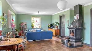 Een gezellige woonkamer met een blauwe bank, een houten eettafel, een open haard en diverse planten.