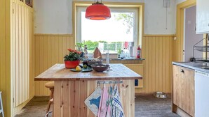 Een keuken met houten kasten, een houten kookeiland met een spoelbak, een rode hanglamp en een raam met uitzicht op groen.