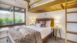 Ein Zimmer mit einem Etagenbett, einem großen Fenster mit Blick auf Grünflächen, einem Nachttisch mit Lampe und einem ordentlich bezogenen Bett.