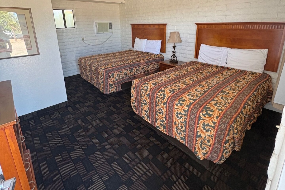 Una habitación con dos camas, un cabecero de madera, una mesita con lámpara y un aire acondicionado instalado en la pared.